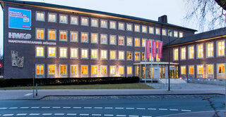 Das Bild zeigt das Gebäude der Handelskammer in Münster bei Dämmerung, erkennbar an der modernen Architektur und beleuchteten Fenstern.