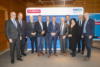 Das Bild zeigt eine Gruppe von Männern und einer Frau, die zusammen für ein Foto posieren. Sie scheinen Teilnehmer einer Veranstaltung zu sein.