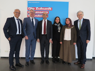 Das Bild zeigt eine Gruppe von sechs Personen, die vor einem Plakat mit dem Slogan „Die Zukunft in unseren Händen“ stehen. Alle lächeln freundlich.