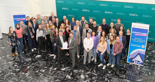 Das Bild zeigt eine große Gruppe von Menschen in einem modernen Raum, die zusammen für ein Projekt namens "Klimafit Ruhr" posieren.