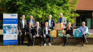 Das Bild zeigt eine Gruppenaufnahme von Fachleuten vor einer grünen Kulisse, umgeben von Symbolen für nachhaltige Entwicklungsziele.