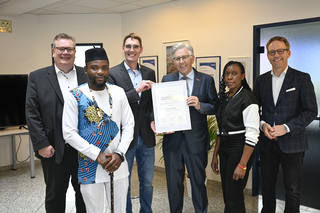 Auf dem Bild sind fünf Personen in einem modernen Büro zu sehen. Sie halten ein Zertifikat und lächeln in die Kamera.