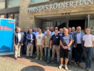 Eine Gruppe von Männern steht vor dem "Haus des Kölner Handwerks". Sie lächeln in die Kamera, einige tragen Namensschilder.